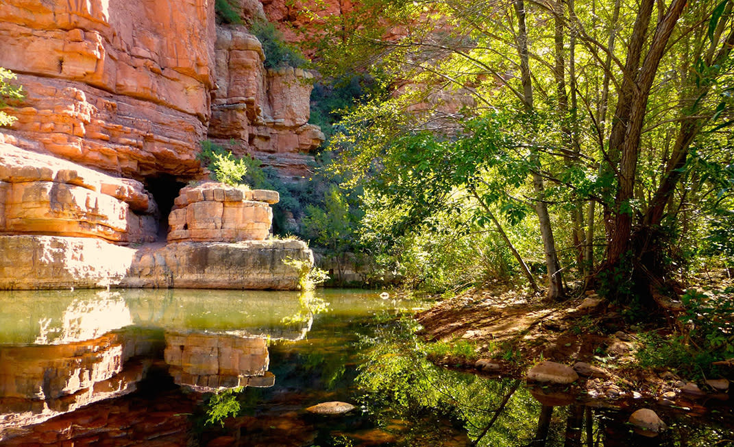 A creek and green trees beneath red rock cliffs along an Arizona trail